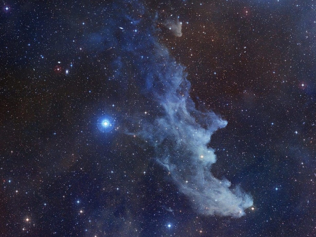 Como su nombre indica, esta nebulosa de reflexión asociada con la estrella Rigel se parece sospechosamente a una anciana de cuento de hadas. Conocida como IC 2118 en la constelación de Orión, la Nebulosa Cabeza de Bruja brilla principalmente por la luz reflejada por la estrella Rigel. El color azulado de esta nebulosa se debe no solo al color azul de su estrella, sino también a que los granos de polvo reflejan la luz azul de manera más eficiente que la roja. Un proceso físico similar hace que el cielo diurno de la Tierra se vea azul.