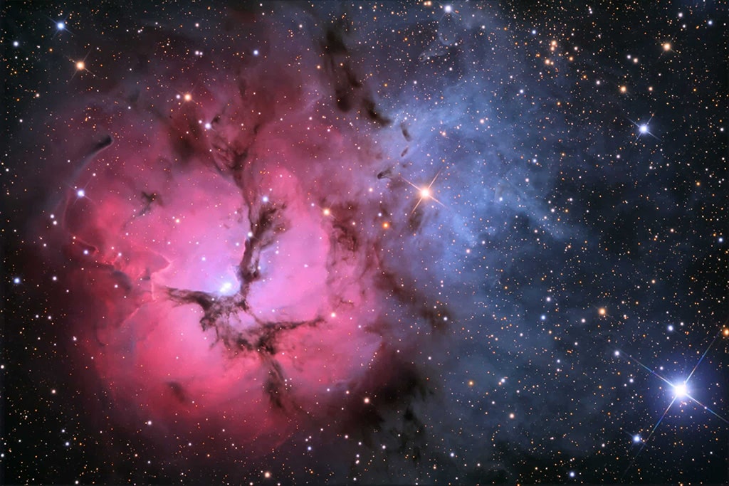 La Nebulosa Trífida, también conocida como M20, es visible con binoculares hacia la constelación de Sagitario. Los procesos energéticos de formación estelar crean no solo los colores sino también el caos.