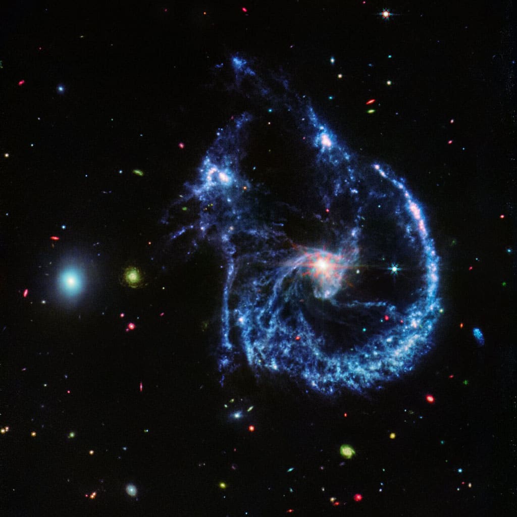 Esta imagen de Arp 107, obtenida por el MIRI (Instrumento de Infrarrojo Medio) del telescopio Webb, revela el agujero negro supermasivo que se encuentra en el centro de la gran galaxia espiral a la derecha de la imagen, evidenciado por el pequeño y brillante ‘núcleo’ central.