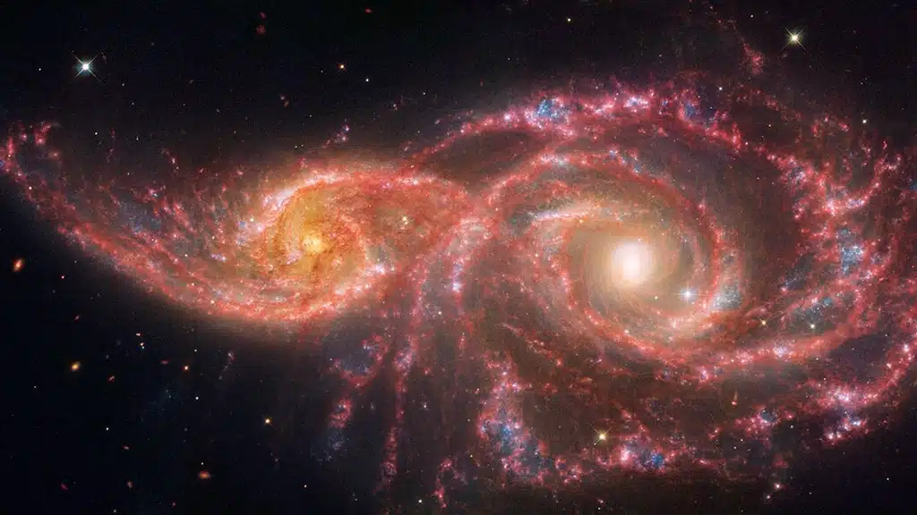 La espeluznante paleta de colores de esta pareja de galaxias se debe a una mezcla de luz del infrarrojo medio, captada por el Telescopio Espacial James Webb, y luz visible y ultravioleta captada por el Telescopio Espacial Hubble de NASA/ESA. La pareja de galaxias se rozó hace millones de años: la espiral menor a la izquierda, catalogada como IC 2163, pasó detrás de NGC 2207, la galaxia espiral más grande a la derecha.