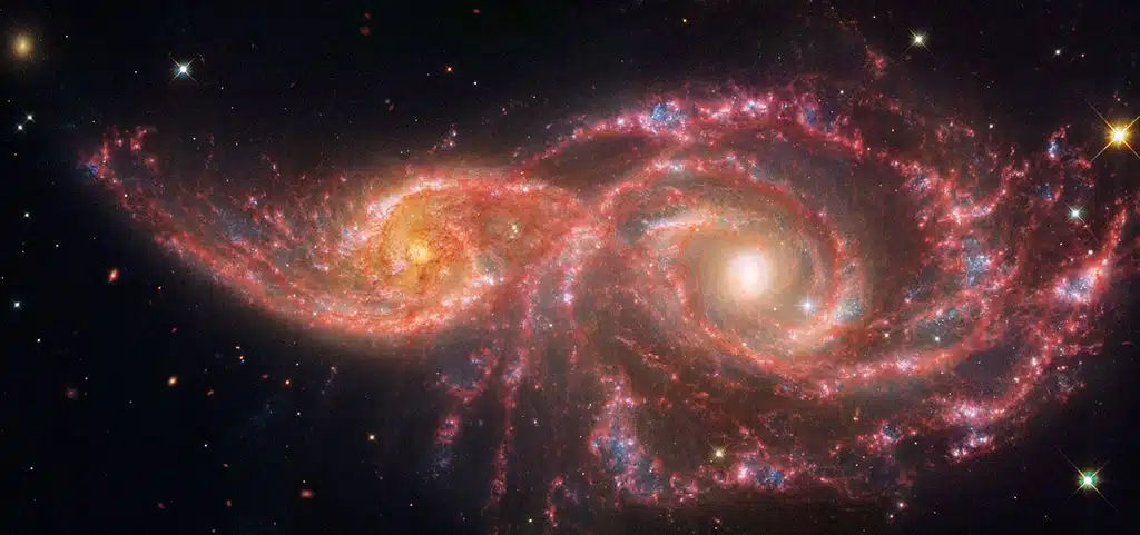 La espeluznante paleta de colores de esta pareja de galaxias se debe a una mezcla de luz del infrarrojo medio, captada por el Telescopio Espacial James Webb, y luz visible y ultravioleta captada por el Telescopio Espacial Hubble de NASA/ESA. La pareja de galaxias se rozó hace millones de años: la espiral menor a la izquierda, catalogada como IC 2163, pasó detrás de NGC 2207, la galaxia espiral más grande a la derecha.