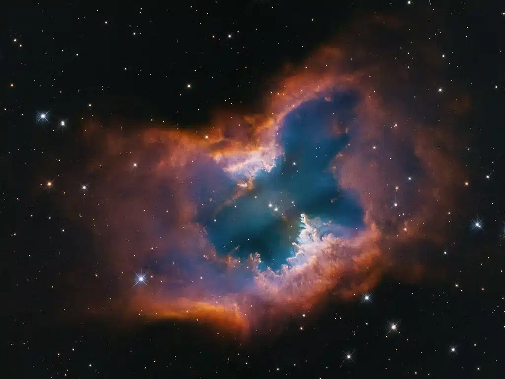 Esta imagen del Telescopio Espacial Hubble captura la belleza de la nebulosa planetaria NGC 2899, que recuerda la forma de una polilla. Este objeto presenta un flujo diagonal, bipolar y cilíndrico de gas, impulsado por la radiación y los vientos estelares de una enana blanca a casi 22.000 grados Celsius en su centro. De hecho, podría haber dos estrellas compañeras que interactúan y modelan la nebulosa, la cual está comprimida en el centro por un anillo o toro fragmentado, con apariencia de un donut a medio comer. Presenta un bosque de “pilares” gaseosos que apuntan hacia la fuente de radiación y vientos estelares. Los colores provienen del brillo del hidrógeno y del oxígeno. La nebulosa se encuentra a aproximadamente 4.500 años luz en la constelación austral de Vela.