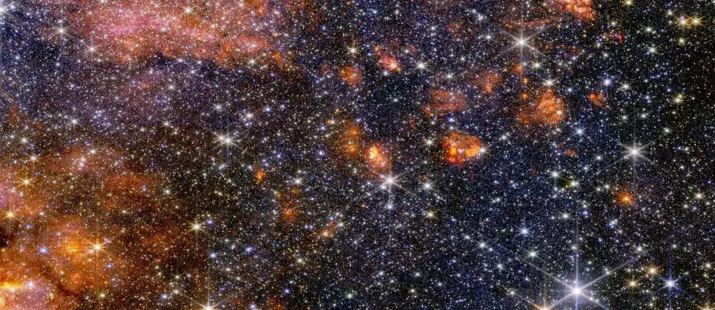 El instrumento NIRCam (Near-Infrared Camera) del Webb muestra estrellas, gas y polvo cósmico en la nube molecular Sagitario B2 brillando en luz infrarroja cercana. En esta luz, los astrónomos observan mejor la diversidad y el colorido de las estrellas de la región, pero perciben menos la estructura de su gas y polvo.