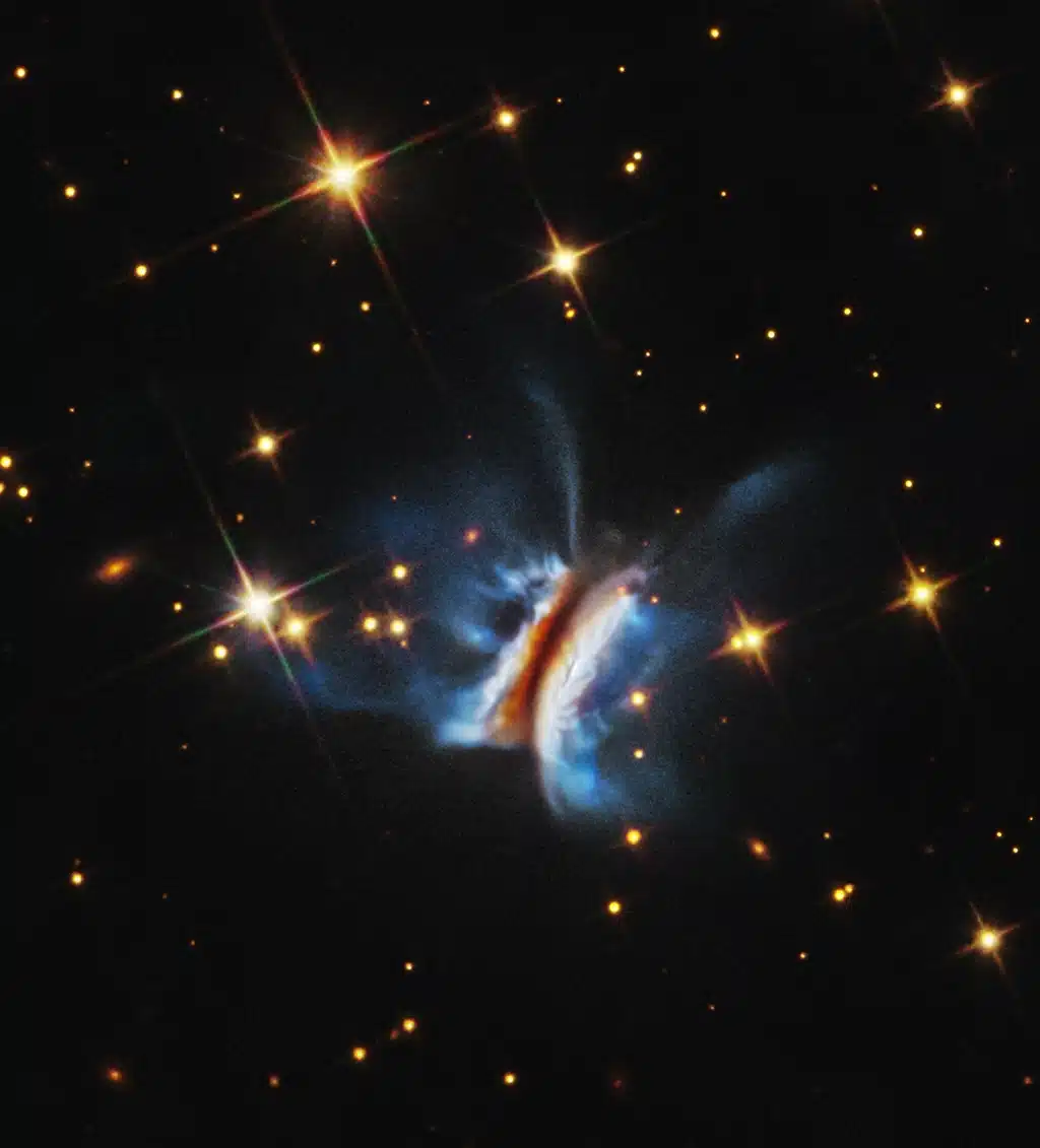Imagen del Telescopio Espacial Hubble del mayor disco protoplanetario jamás observado alrededor de una estrella joven. Filamentos brillantes se extienden muy por encima y por debajo del disco, más de lo observado en cualquier otro disco circumestelar similar.