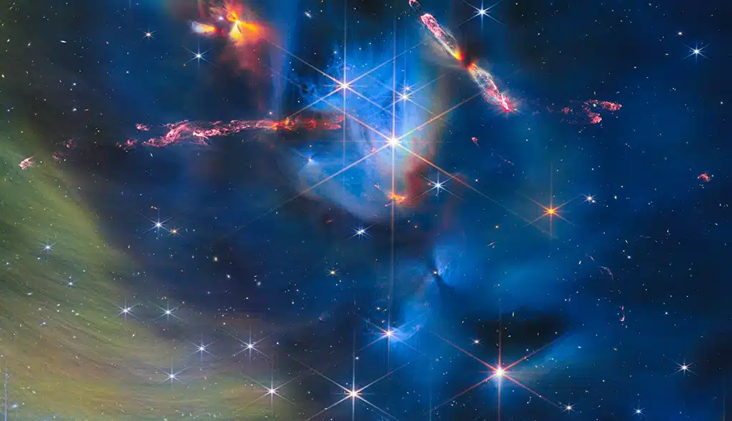 Esta imagen del Webb muestra estrellas y protoestrellas en las proximidades del cúmulo estelar IC 348. El objeto largo y estrecho orientado horizontalmente en el lado izquierdo de la imagen es HH 797. Al observarlo de cerca, se revela que esta fuente está formada por dos protoestrellas con flujos de salida casi paralelos. A la derecha, y dispuesto en diagonal, se encuentra la fuente HH 211, con forma de hélice, que presenta tanto chorros estrechos como flujos de salida más amplios y que también apareció en una publicación anterior de imágenes. La zona naranja brillante situada directamente sobre HH 797, denominada LLRL 54361 se cree que alberga otras dos protoestrellas. En esta nebulosa se ocultan otras protoestrellas, más o menos inmersas en el material circundante, que contribuyen a los bordes y a los patrones ondulados de las nubes, además de generar otros espectaculares flujos de salida brillantes. Las tenues cortinas de la parte inferior izquierda de la imagen son material interestelar que refleja la luz de las estrellas del cúmulo: lo que se conoce como una nebulosa de reflexión. El material también contiene moléculas con carbono conocidas como hidrocarburos aromáticos policíclicos, o HAP.
